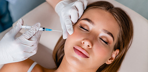 a young woman receiving a facial injection from a white-gloved beautician in a salon
